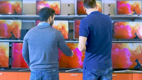 In the Electronics Store Professional Consultant Shows Latest 4K UHD TV's to a Young Man, They Disc