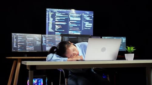 Une programmeuse asiatique dort pendant qu'elle écrit du code sur un ordinateur portable à l'aide de plusieurs moniteurs
