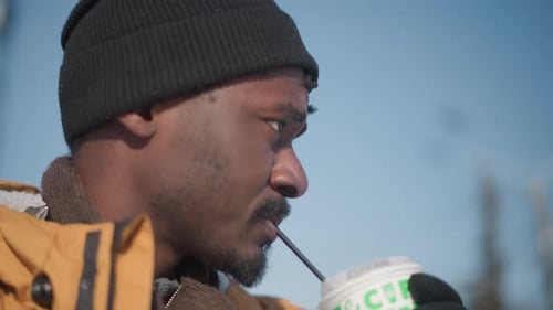 Reporter in Yellow Coat Sipping Juice Holding Camera on Snowy Street