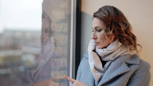 Beautiful Lady in Blue Coat Looking at Window in Winter or Spring Day Romantic and Pensive Face