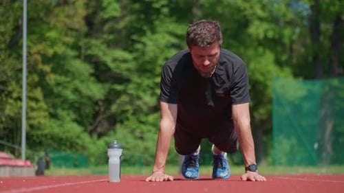 Man Doing Pushups on Stadium Track During Training Session