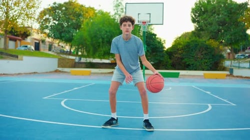 Boy Dribbling Basketball on Blue Outdoor Court
