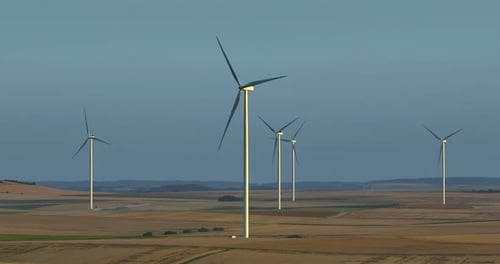 Alternative Energy Large Wind Turbines with Blades in Field Aerial View Bright Orange Sunset Blue
