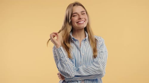 Smiling Young Woman Twirling Hair on Yellow Background