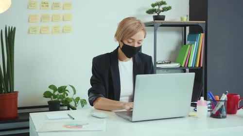 Young Woman Employee in a Medical Facial Mask Works in the Office Use Laptop Coronavirus Pandemic