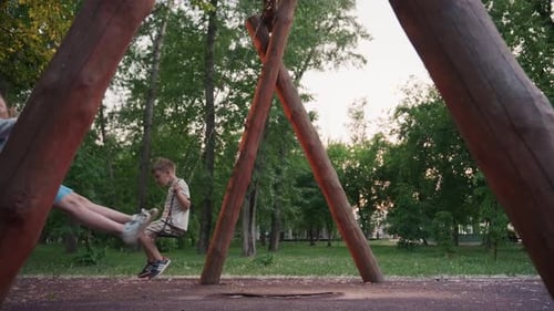 Playmates Swinging in Opposite Directions at Dusk in Leafy Park