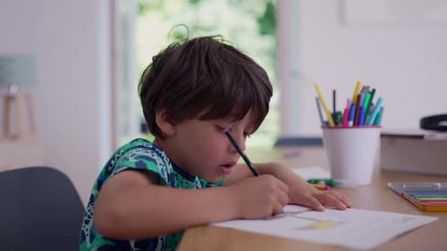 Der Junge konzentrierte sich darauf, mit einem Bleistift zu zeichnen, saß an einem Tisch, umgeben von bunten Markierungen und