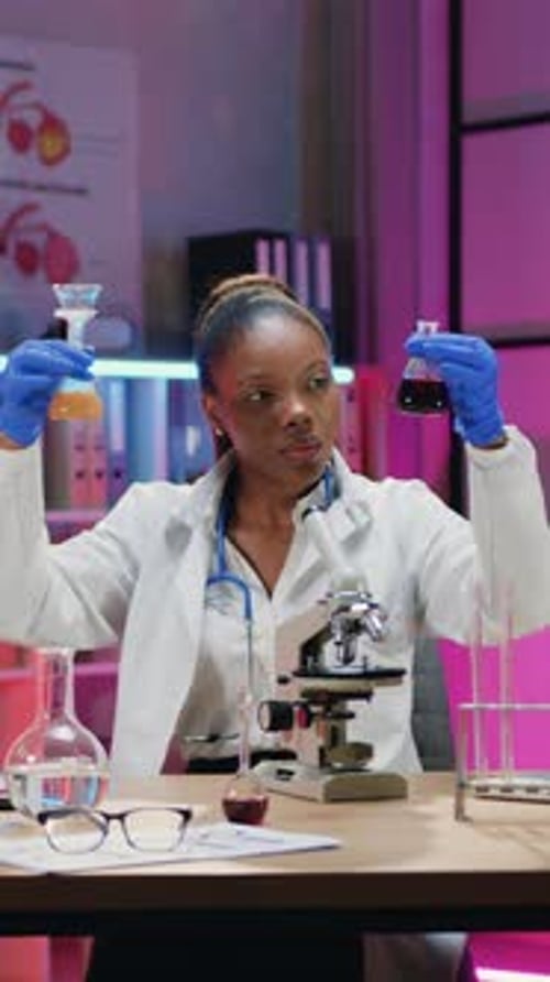 Scientifique afro-américaine expérimentée assez concentrée en uniforme médical et protectrice