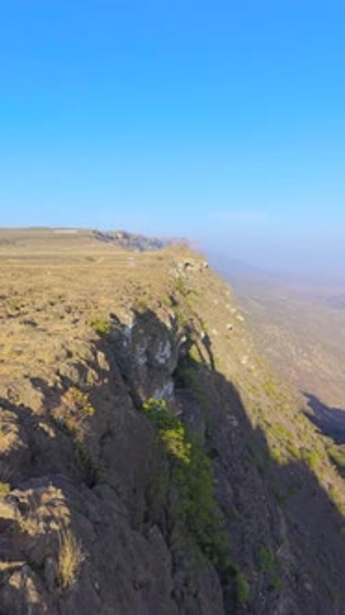 Aerial View of a Young Woman Wearing a Red Dress Standing on a Rocky Cliff Edge Overlooking a Wide