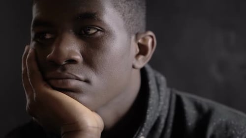 Thoughtful bored young american african man thinking alone in the dark