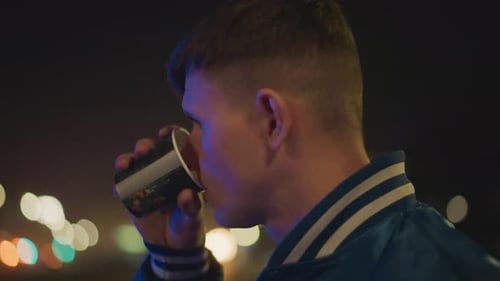 Young Man Drinking from Cup at Night