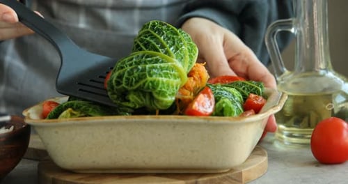 Woman with stuffed cabbage rolls at grey table, closeup