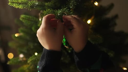 Child Decorates Christmas Tree with Green Ornament
