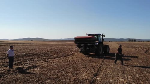 Farmers Working Near Tractor on Dry, Rural Field