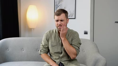 Young Handsome Man at Home Touching Mouth with Hand with Painful Expression Because of Toothache or