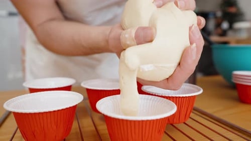 A woman squeezes the batter from the bag into the red cupcake liners for baking.