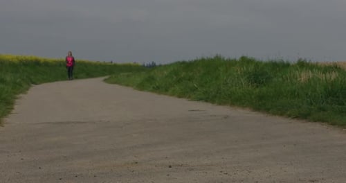 Older woman exercise walking around a corner on field road in distance in afternoon
