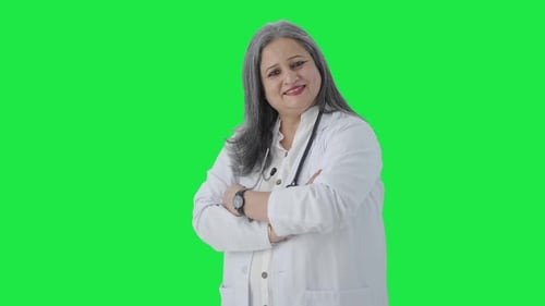 Happy Indian senior female doctor standing crossed hands Green screen