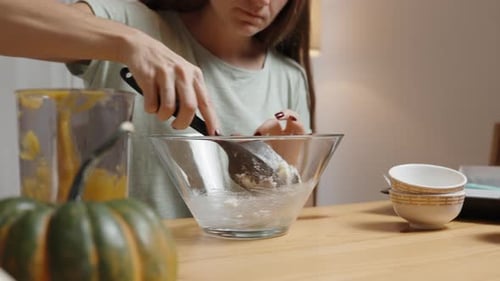 Young Woman Stirs Some White Mixture in a Bowl. She's Cooking Dinner with a Pumpkin on the Table.
