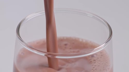 Close Up Of Slow Motion Pour Chocolate Milk Drink In Tumbler Glass On White Background