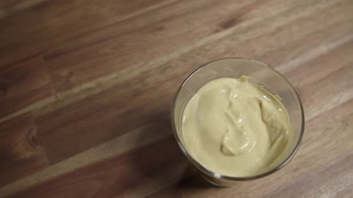 Medium close shot of yellow mustard sitting in a small glass jar. Top shot, panning. Nobody, studio.