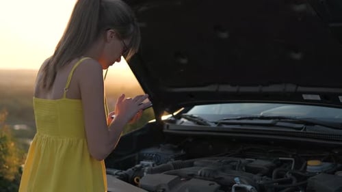 Young Woman Driver Talking on Mobile Phone Standing Near Her Car with Open Hood Having Motor Problem