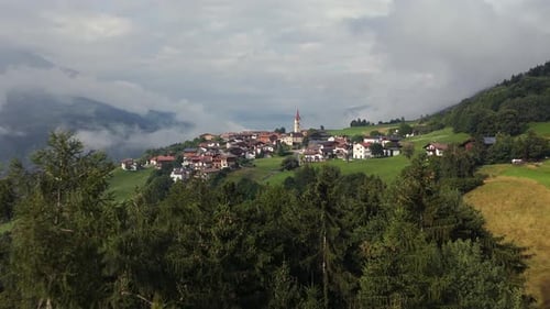 A picturesque village perched on a hill, surrounded by lush forests and misty mountains, under a par