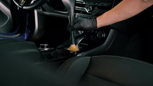 Car wash worker thoroughly cleaning the interior of a luxury car with a brush, gear box, detailing