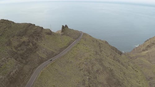 Panorama drone shot of a car driving through a road in the mountains and ocean in the background