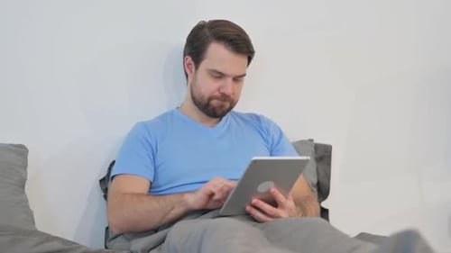 Man Using Tablet in Bed at Home