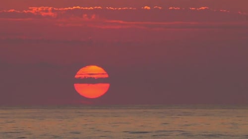 Big orange sun rising above calm sea at dawn, ocean sunrise