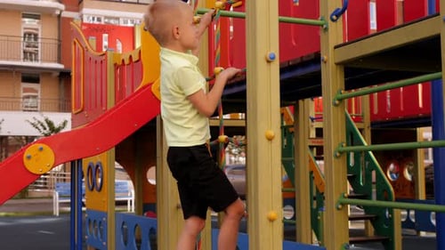 A Child Climbs a Grid in a Park on a Playground on a Hot Summer Day