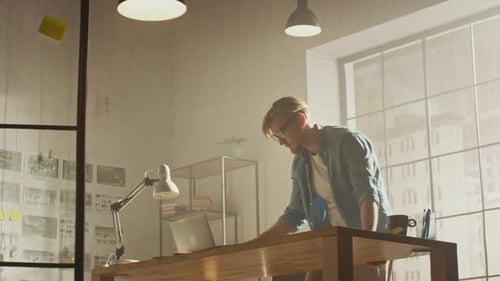Low Angle Shot: Young Creative Designer Works in His Studio Office, uses Laptop, Browses Through Pr