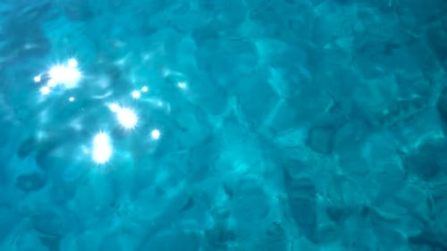 Shiny ocean blue waves with the glistening sun reflecting on the surface. Filmed from straight above