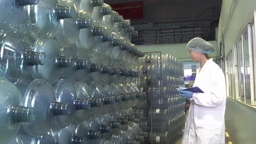 Technologue dans une usine d'embouteillage vérifiant les bouteilles d'eau avant expédition.