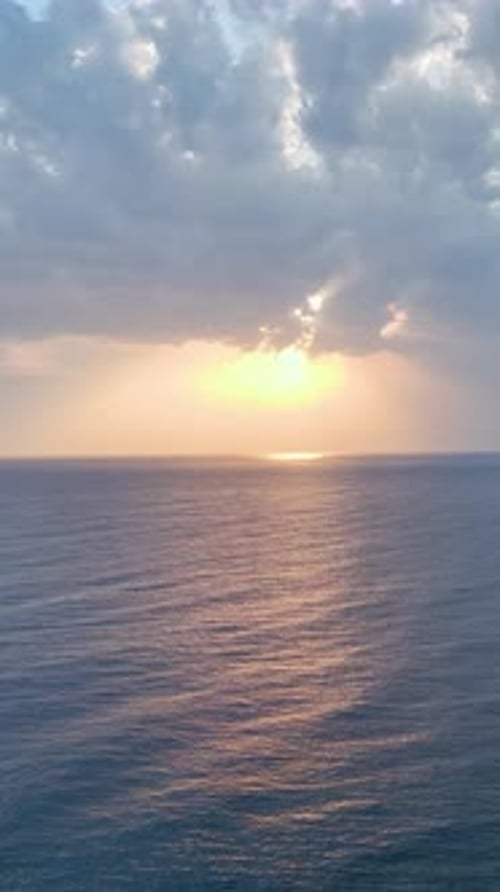 Vidéo aérienne verticale d'une scène océanique magique avec des nuages et des rayons de soleil se reflétant sur l'eau