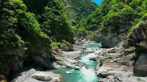 Aerial establishing flight over flowing stream between rocks surrounded by green nature