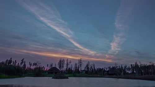 Rural cabin in a winter landscape at sunset with the lake water freezing on the ice - colorful, wide