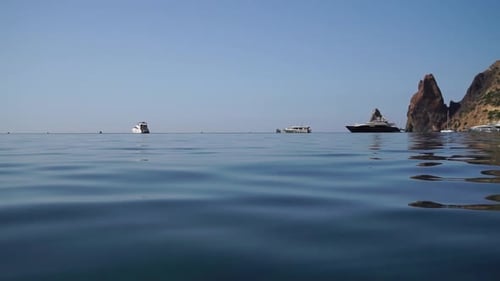 Sea Water Surface Camera Flies Over the Calm Azure Sea with Volcanic Rocky Shores on Background