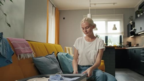 Young woman packing suitcase in living room daytime