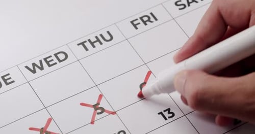 Hand Marking Days on White Calendar with Red Marker