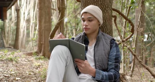 Young man in forest writing in notebook, reflecting on nature's beauty