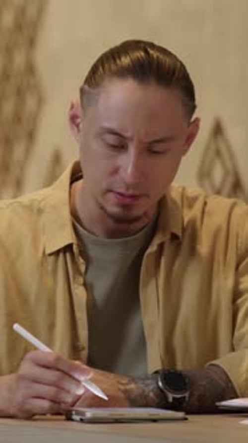 Man Using Stylus on Tablet at Indoor Table