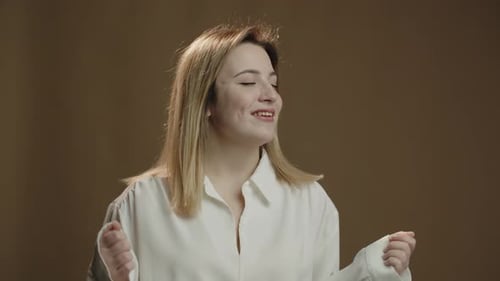 Excited Blonde Woman Dancing and Singing on Dark Background Studio Footage of Happy Girl in White