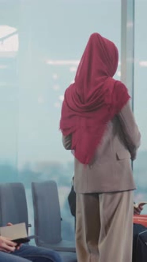 Serene Woman Wearing Hijab Reviews Travel Documents While Seated Among Fellow Travelers in Airport