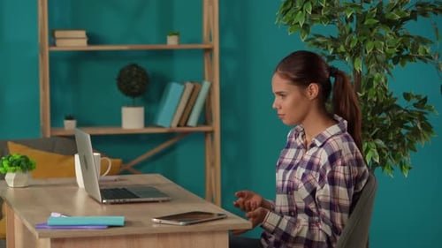 Medium Shot Capturing a Woman Having a Videocall Talking to Somebody on a Laptop in Her Home Office