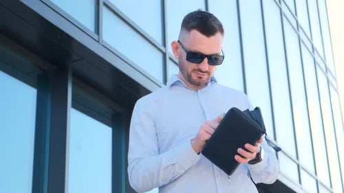 A Stylish Businessman is Counting Money in His Wallet He is Wearing a Blue Shirt and Sunglasses
