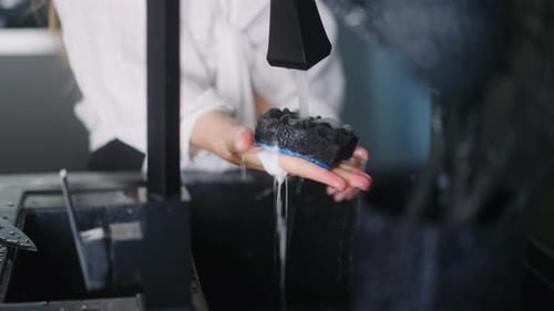 Espremer uma esponja espumante para lavar louça com detergente na mão de uma mulher caucasiana sobre um escuro moderno