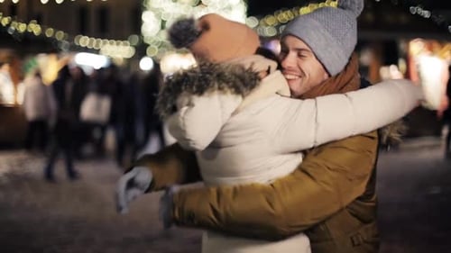 Happy young couple meeting and embracing at christmas market on winter evening