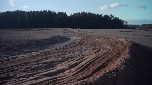 A guy riding a motorcycle on a motocross track, splashing dirt as he goes by. Video taken next to a